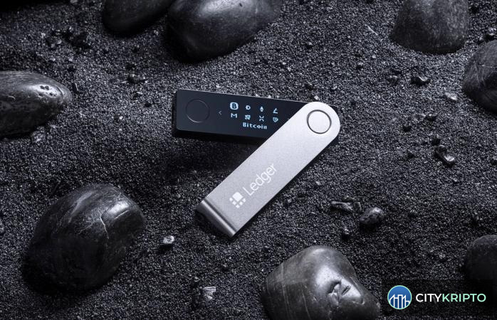 Аппаратный кошелёк Ledger и символы криптовалют Bitcoin, Ethereum, Tron на фоне взлома