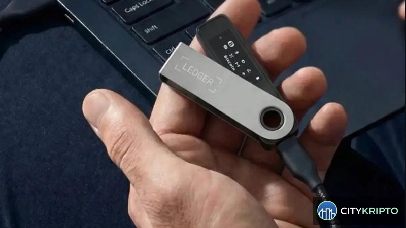 Аппаратный кошелёк Ledger и логотип CryptoBilis на фоне криптовалютных графиков