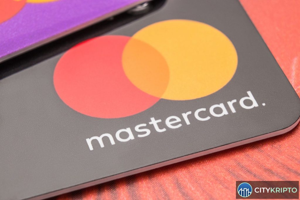 Логотип Mastercard и символы криптовалют на фоне графиков финансового рынка